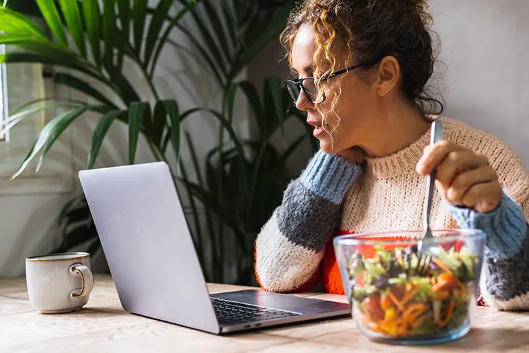 Woman working at computer while eating salad